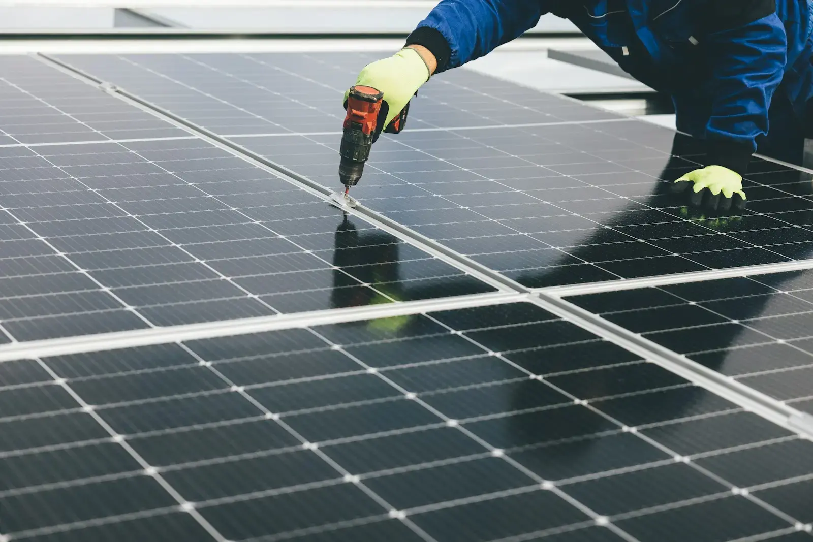 Des mains gantées fixent à la visseuse un module photovoltaïque sur une toiture